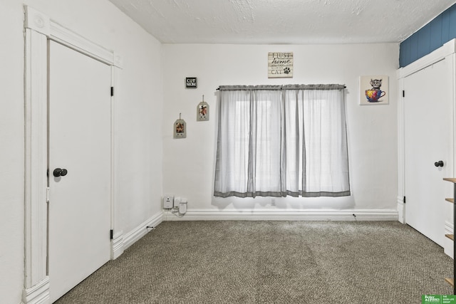 unfurnished room featuring a textured ceiling and dark colored carpet