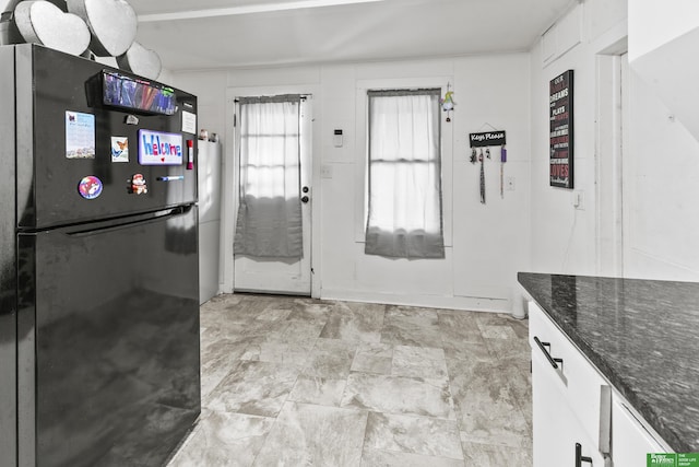 kitchen featuring black fridge, dark stone counters, and white cabinets