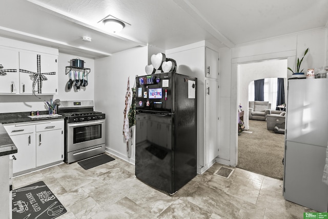 kitchen featuring stainless steel gas range, white cabinetry, black refrigerator, fridge, and light colored carpet