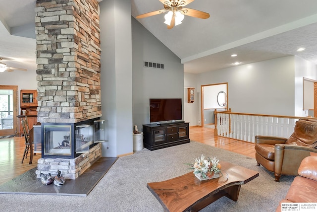 carpeted living room featuring ceiling fan, a stone fireplace, and high vaulted ceiling