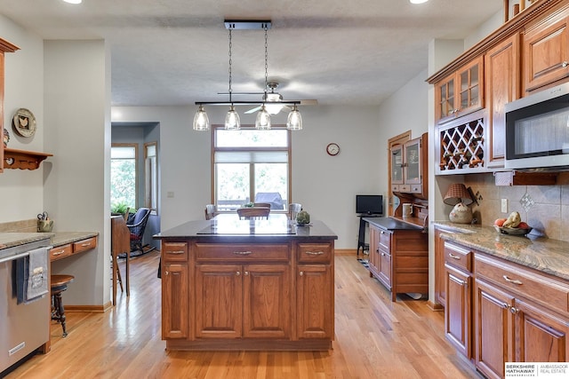 kitchen featuring dark stone countertops, light hardwood / wood-style floors, decorative backsplash, a kitchen island, and decorative light fixtures