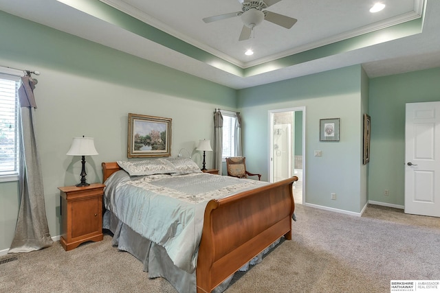 carpeted bedroom with connected bathroom, a tray ceiling, ornamental molding, and ceiling fan