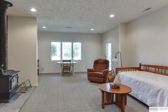 bedroom featuring light carpet, a textured ceiling, and a wood stove