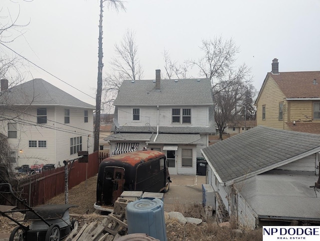 rear view of property with a shingled roof and fence