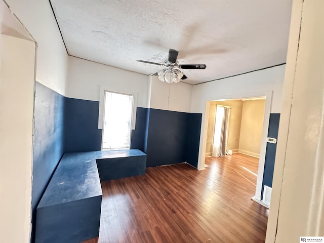 empty room with a textured ceiling, visible vents, wood finished floors, and a ceiling fan