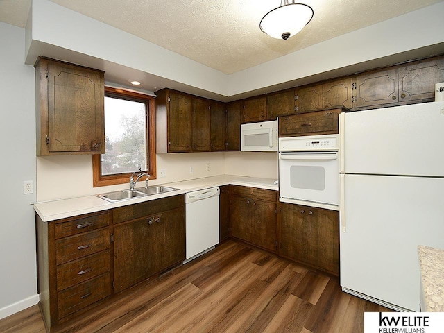 kitchen with dark brown cabinetry, sink, a textured ceiling, dark hardwood / wood-style flooring, and white appliances