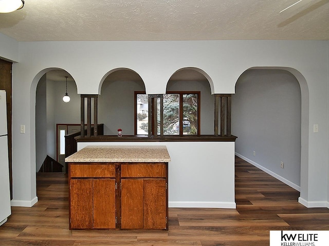 kitchen featuring dark wood-type flooring, a textured ceiling, white fridge, a kitchen island, and pendant lighting