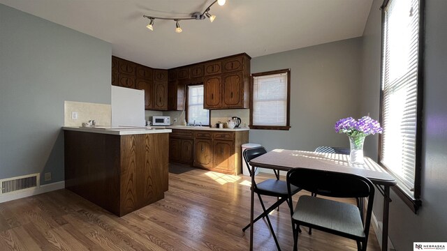 kitchen featuring light countertops, white microwave, a peninsula, and wood finished floors