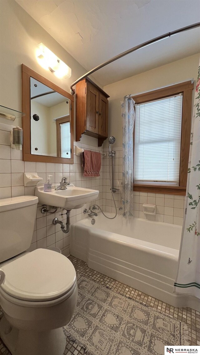 bathroom with shower / tub combo with curtain, tile walls, toilet, a sink, and tile patterned flooring