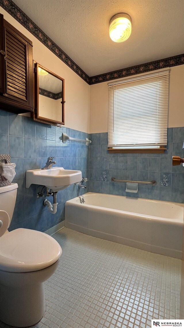 full bath with a textured ceiling, toilet, tile walls, a bath, and tile patterned floors