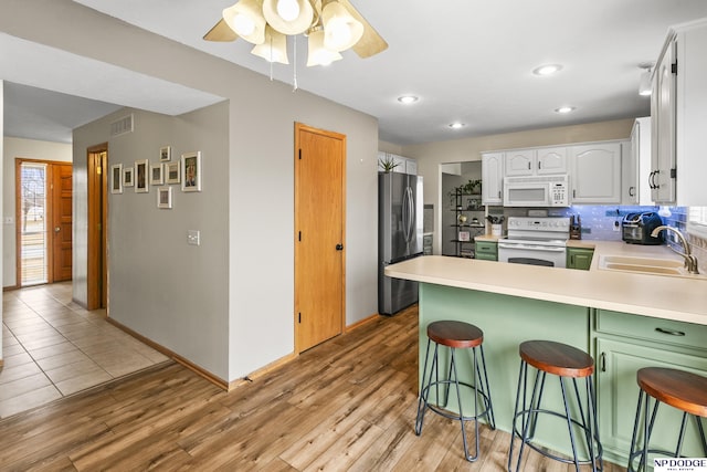 kitchen featuring sink, white appliances, white cabinetry, a kitchen breakfast bar, and kitchen peninsula