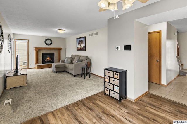 living room with a tiled fireplace, wood-type flooring, and ceiling fan