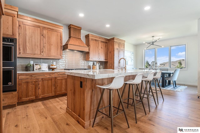 kitchen featuring a breakfast bar, sink, custom exhaust hood, a center island with sink, and backsplash