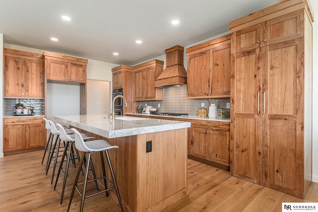 kitchen featuring a breakfast bar, sink, custom exhaust hood, stainless steel gas cooktop, and a center island with sink