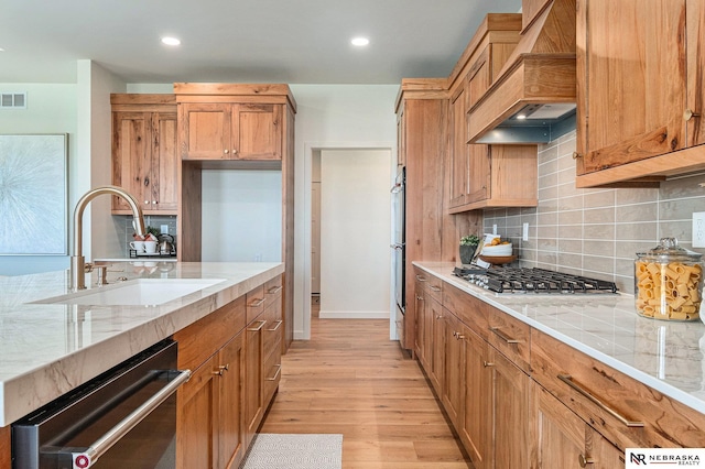 kitchen with sink, backsplash, stainless steel appliances, custom exhaust hood, and light wood-type flooring