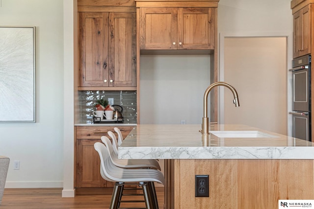 kitchen featuring a breakfast bar, sink, stainless steel double oven, light hardwood / wood-style floors, and backsplash