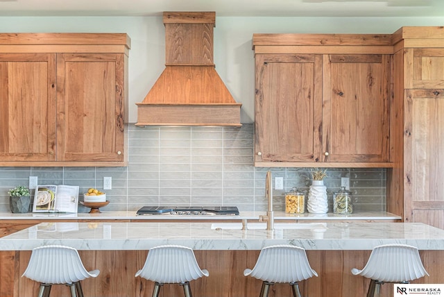 kitchen with tasteful backsplash, a breakfast bar, stainless steel gas cooktop, and custom range hood