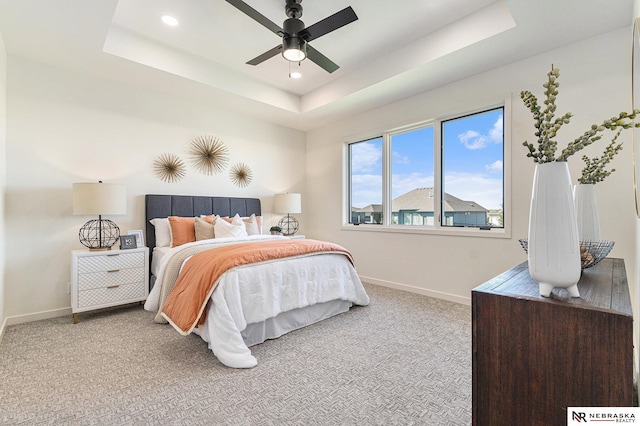 bedroom with light colored carpet, ceiling fan, and a tray ceiling