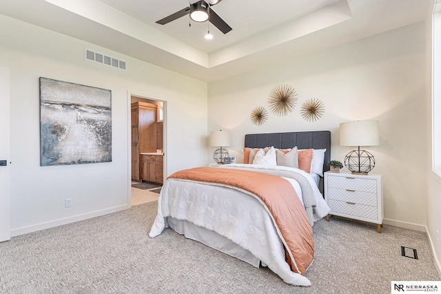 bedroom with ceiling fan, light colored carpet, connected bathroom, and a tray ceiling