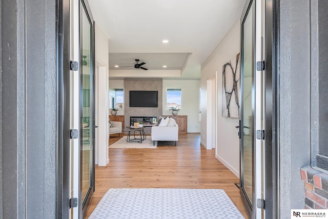 entrance foyer featuring a raised ceiling, ceiling fan, a large fireplace, and light wood-type flooring