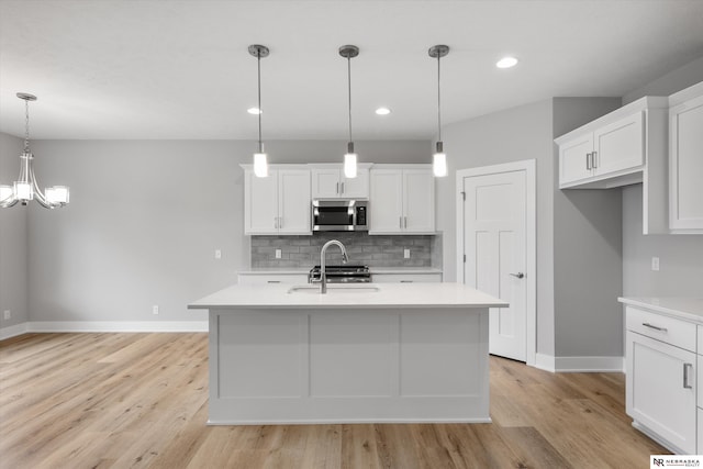 kitchen with a center island with sink, appliances with stainless steel finishes, light countertops, white cabinetry, and pendant lighting