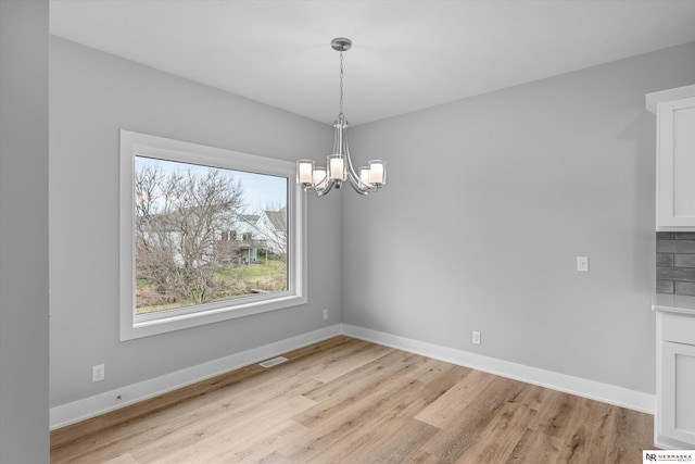 unfurnished dining area featuring baseboards, light wood-style floors, visible vents, and an inviting chandelier