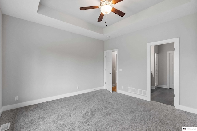 unfurnished bedroom with baseboards, visible vents, a tray ceiling, and dark colored carpet