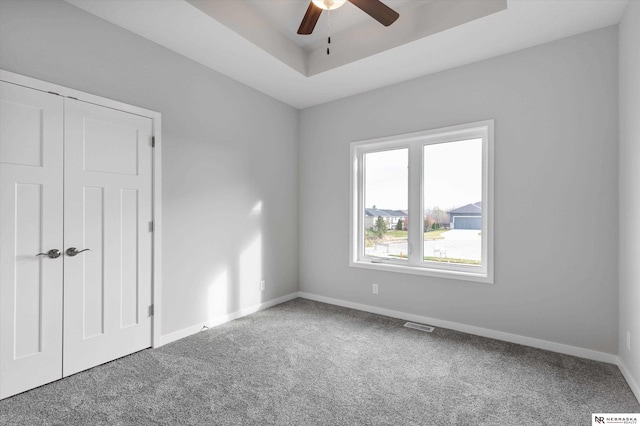 unfurnished bedroom featuring baseboards, visible vents, ceiling fan, carpet, and a tray ceiling