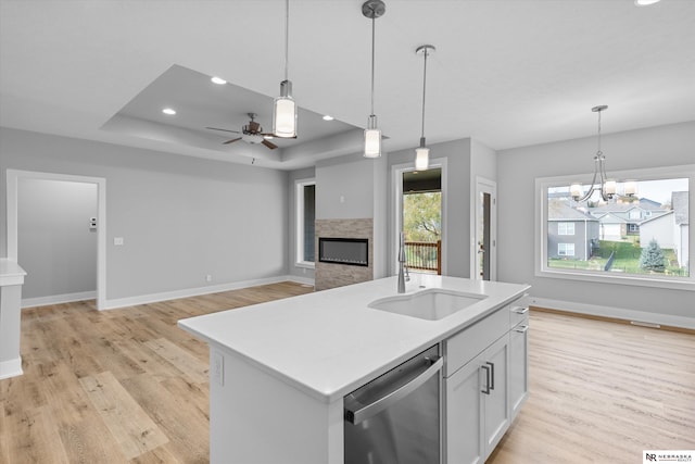 kitchen featuring dishwasher, open floor plan, a kitchen island with sink, a tray ceiling, and a sink