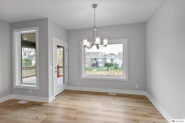 unfurnished dining area with baseboards, visible vents, a chandelier, and light wood-style flooring