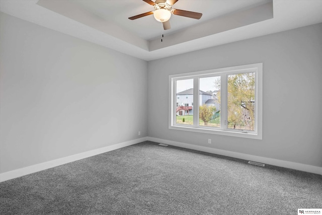 carpeted spare room featuring baseboards, visible vents, a tray ceiling, and a ceiling fan