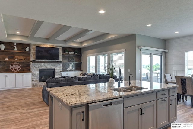 kitchen featuring sink, a kitchen island with sink, stainless steel dishwasher, light stone counters, and light hardwood / wood-style flooring