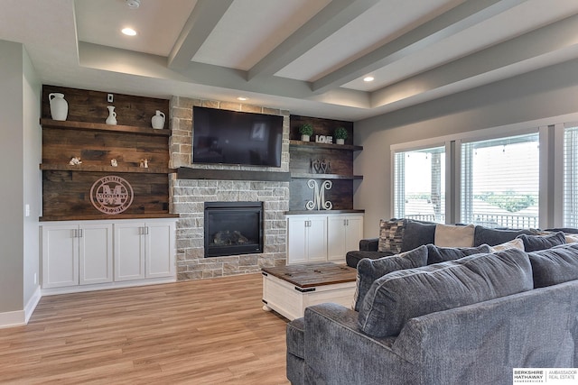 living room with a stone fireplace, light hardwood / wood-style floors, and beamed ceiling