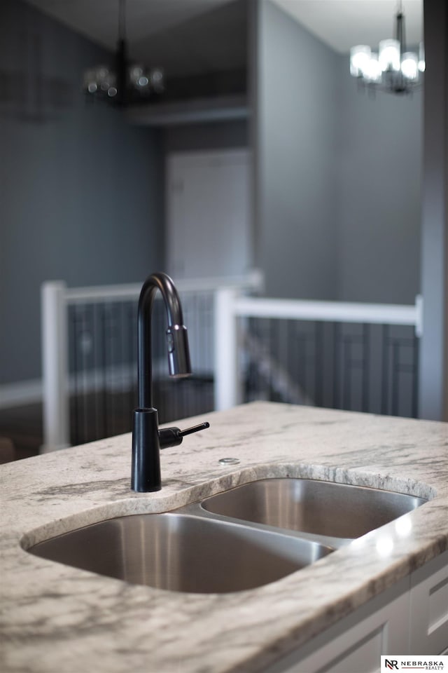 details featuring sink, white cabinets, hanging light fixtures, a notable chandelier, and light stone countertops