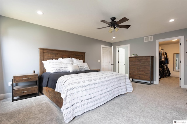 bedroom with a spacious closet, light colored carpet, a closet, and ceiling fan