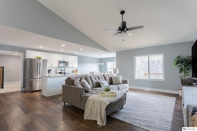 living room with dark wood-type flooring, ceiling fan with notable chandelier, and high vaulted ceiling