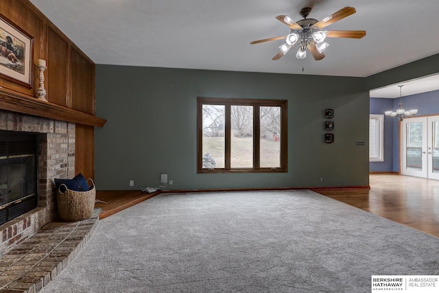 unfurnished living room featuring a brick fireplace, ceiling fan with notable chandelier, and carpet floors