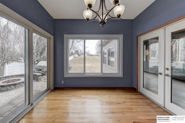 unfurnished dining area featuring french doors, a notable chandelier, and light wood-type flooring