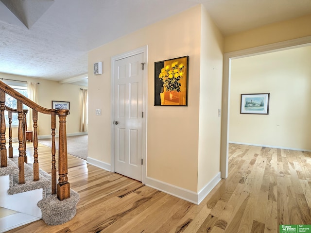 hall with baseboards, stairway, a textured ceiling, and light wood-style floors