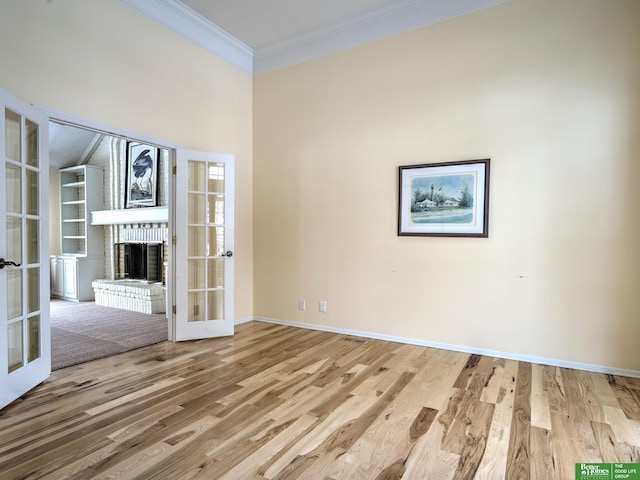 empty room with light wood-style floors, a fireplace, ornamental molding, and french doors