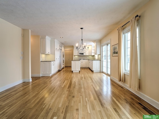 kitchen featuring white cabinetry, decorative light fixtures, light wood finished floors, and white microwave