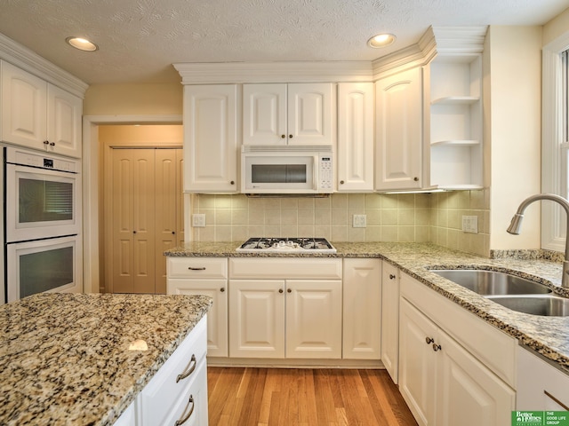 kitchen with white appliances, light stone counters, white cabinetry, open shelves, and a sink