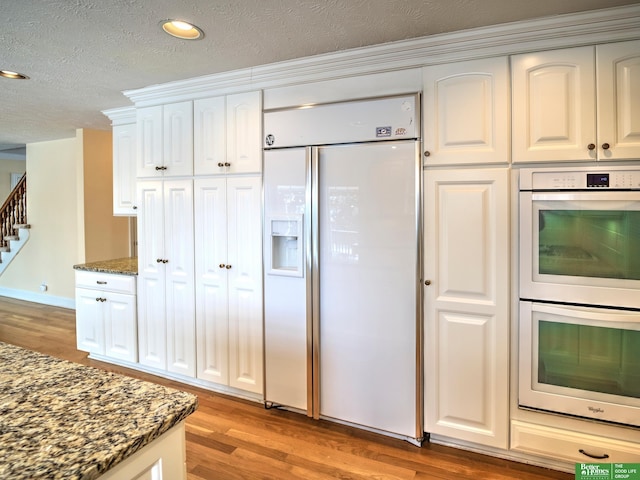 kitchen with white appliances, dark stone countertops, a textured ceiling, light wood-style floors, and white cabinetry