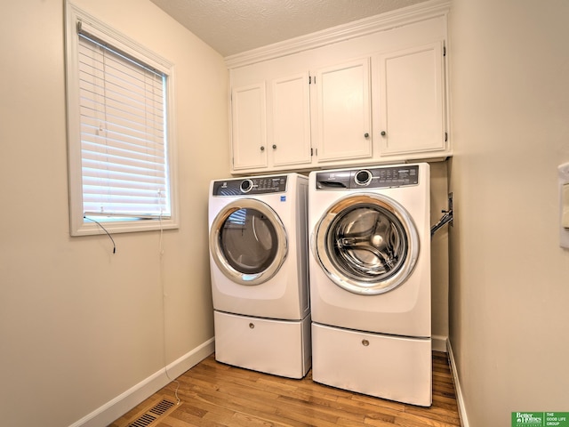 laundry area featuring light wood-type flooring, washing machine and dryer, cabinet space, and baseboards