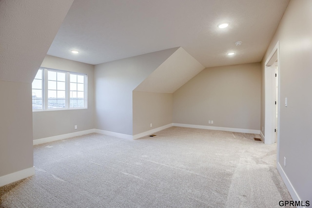 additional living space featuring vaulted ceiling, light carpet, and a textured ceiling