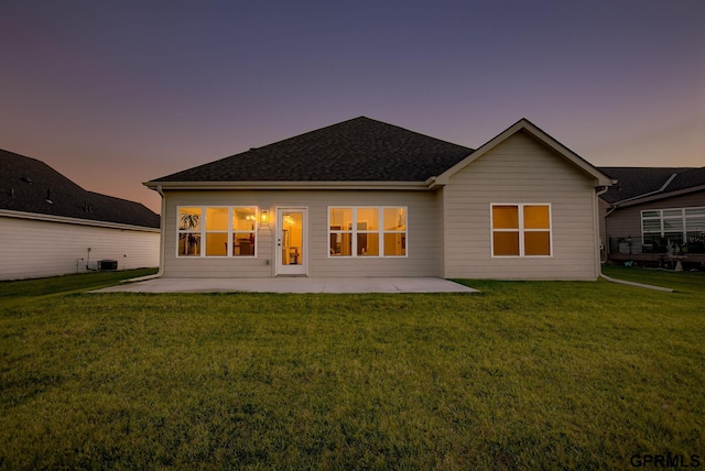 back house at dusk featuring a lawn, central air condition unit, and a patio area