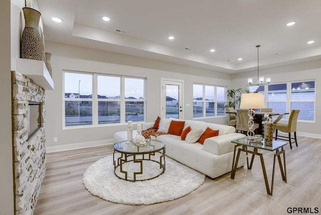 living room featuring a notable chandelier, light wood-type flooring, and a tray ceiling