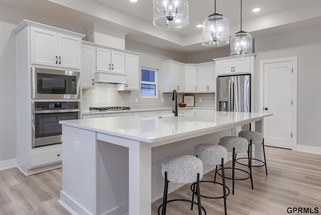 kitchen with white cabinetry, appliances with stainless steel finishes, a center island with sink, and decorative light fixtures