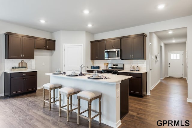 kitchen featuring a breakfast bar, sink, appliances with stainless steel finishes, hardwood / wood-style flooring, and a kitchen island with sink