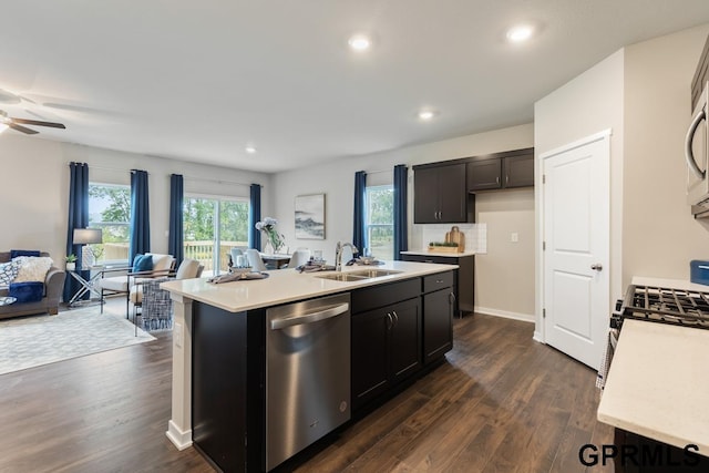 kitchen with appliances with stainless steel finishes, sink, a kitchen island with sink, ceiling fan, and dark wood-type flooring